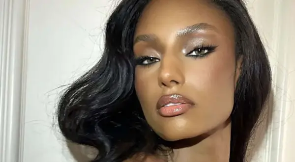 Volto di donna con trucco da sera elegante: occhi definiti da eyeliner e ombretto luminoso, labbra glossate. Capelli scuri e ondulati.