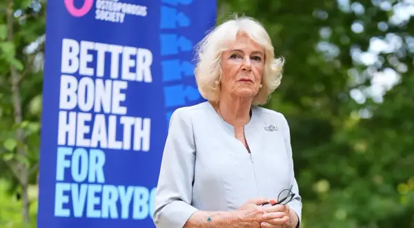 Camilla, regina consorte del Regno Unito, sorride con un banner della Royal Osteoporosis Society alle spalle.