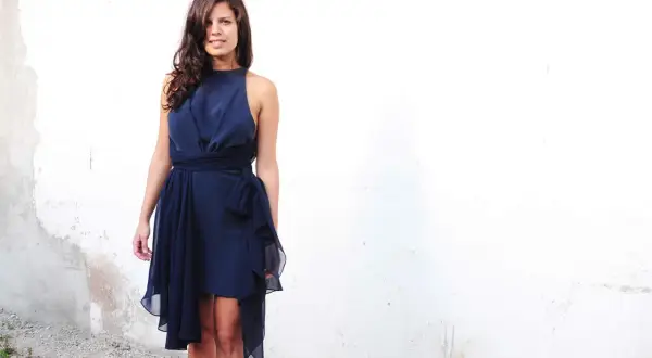 Donna con abito blu notte con drappeggio davanti, vita segnata da una cintura con fiocco.