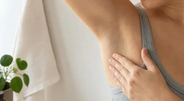 Mano che sfiora l'ascella, un gesto che ci ricorda perchè il sudore puzza e come prendersene cura.