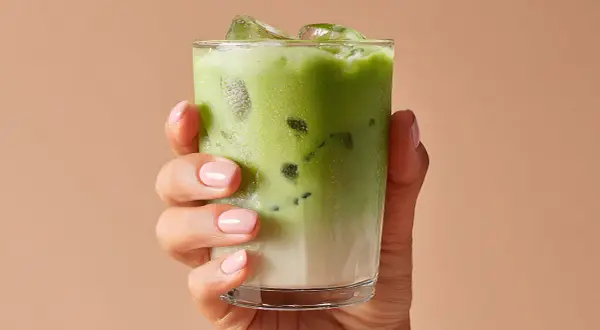 Mano con un bicchiere di matcha ghiacciato. Attenzione alle matcha controindicazioni per goderselo al meglio.