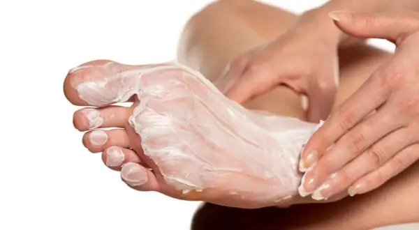Mani che applicano una crema idratante su un piede, creando un impacco per piedi secchi fai da te per una pelle morbida e nutrita.