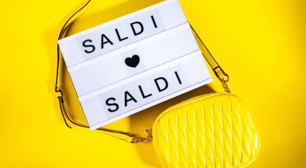 Scatola luminosa con "SALDI" e una borsa gialla. Scopri quanto durano i saldi estivi per fare acquisti convenienti!