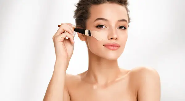 Donna applica fondotinta con pennello. Per un look naturale, il correttore deve essere più chiaro del fondotinta.