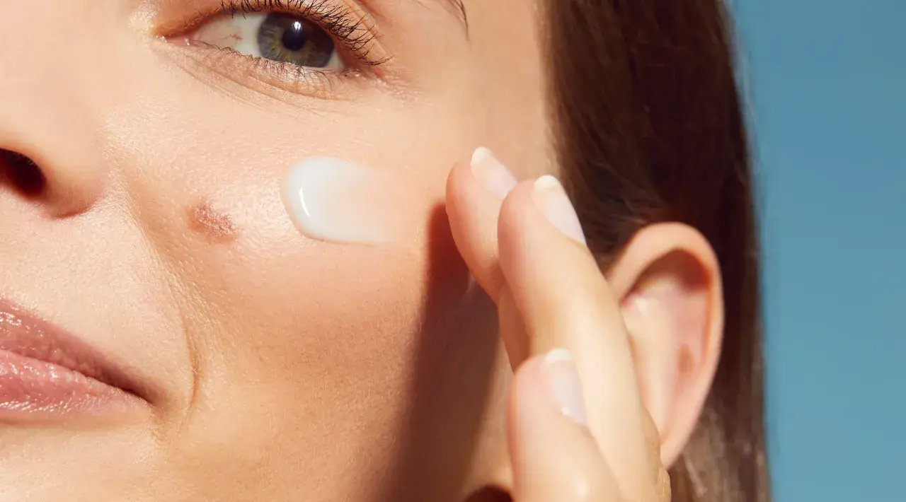 Dito, un dito applica una crema su una pelle ruvida con puntini bianchi, vicino all'occhio e alla bocca.