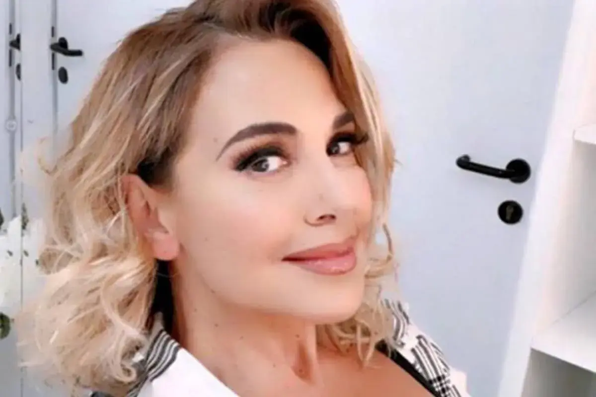 Barbara D'Urso sorride con capelli biondi mossi e trucco accentuato.