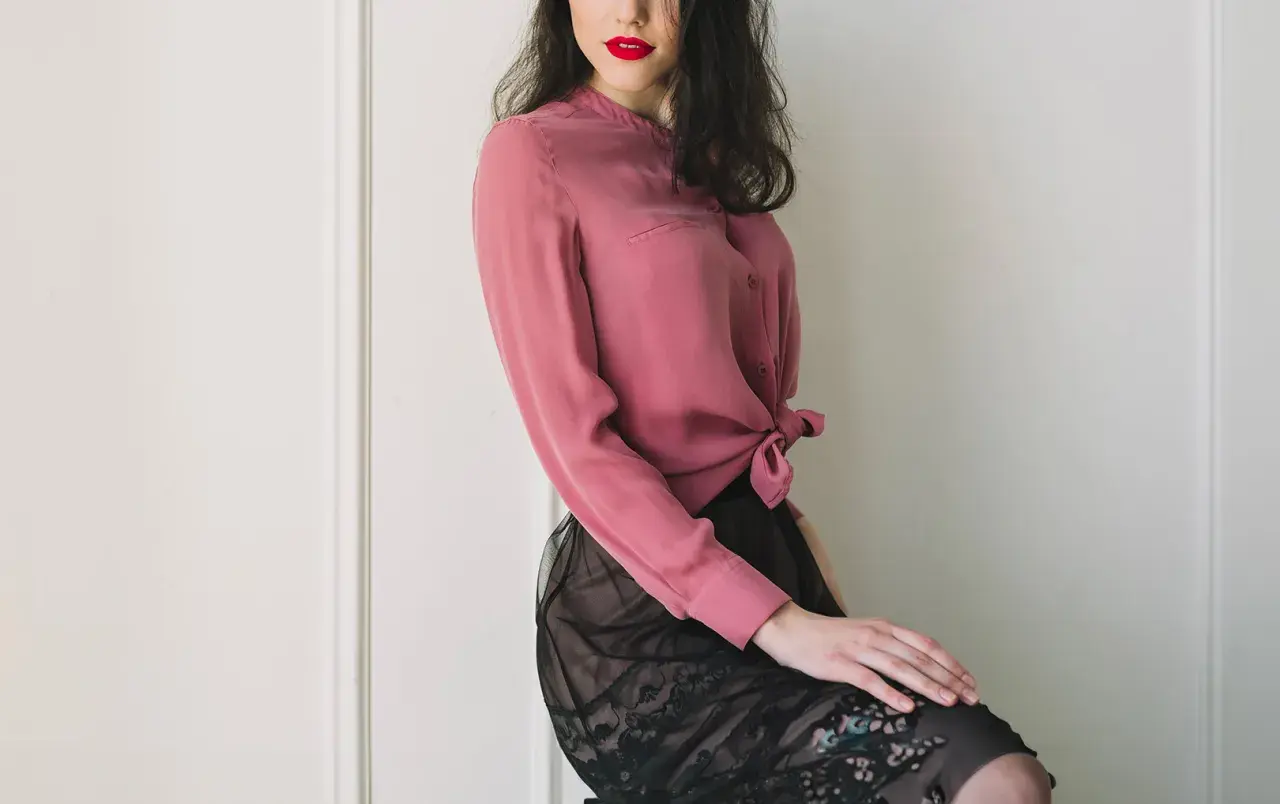 Donna con labbra rosse indossa una blusa in chiffon rosa annodata in vita e una gonna di pizzo nero.