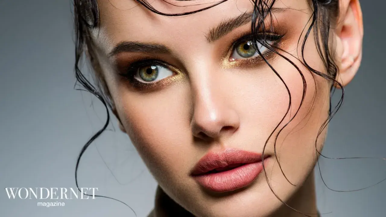 Occhi verdi intensi e labbra sensuali con un audace trucco grafico, capelli bagnati che incorniciano il viso.