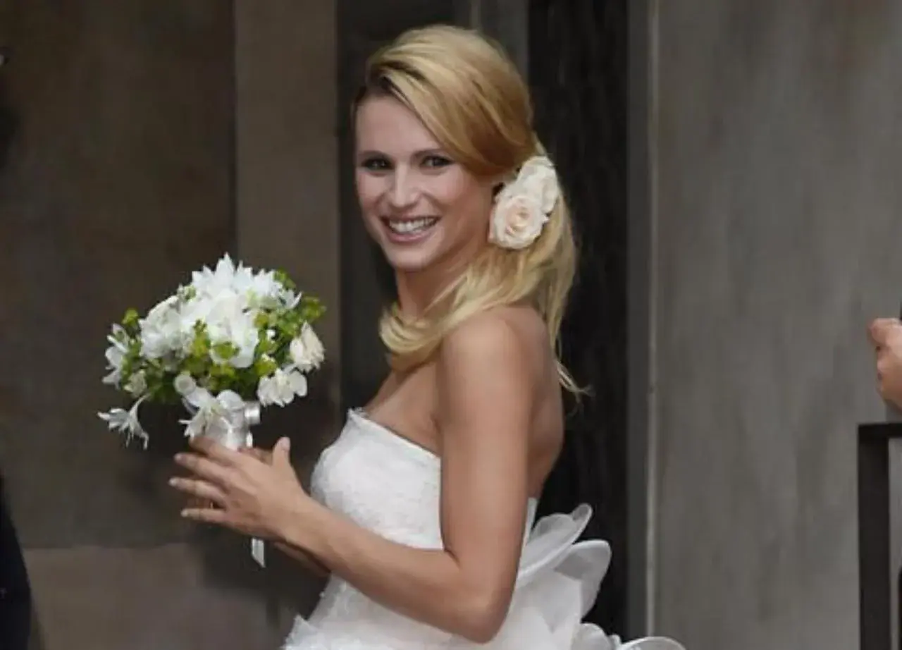 Michelle Hunziker sorride con un bouquet, indossando un abito da sposa che ricorda quello del suo matrimonio con Eros Ramazzotti.