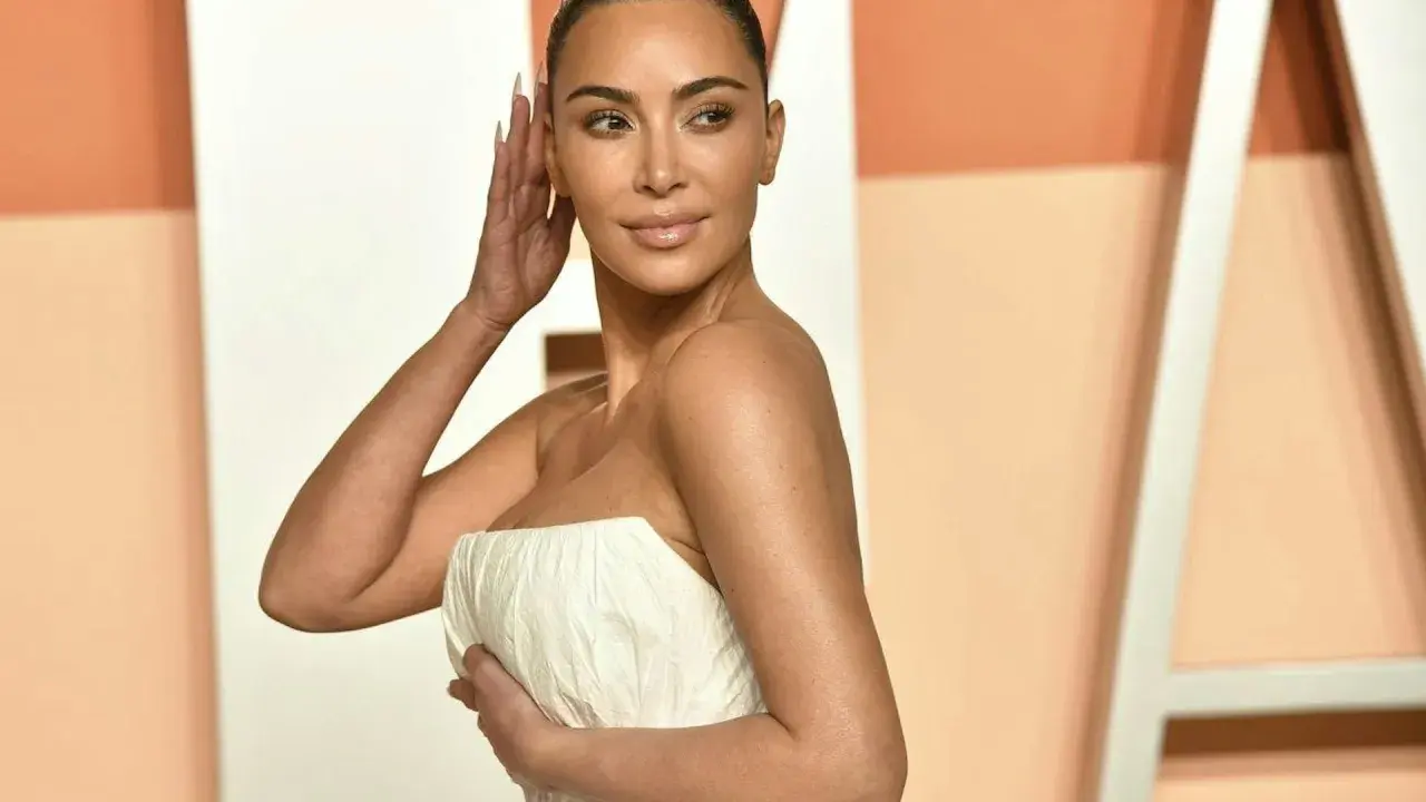 Kim Kardashian con un abito bianco senza spalline, posa con la mano tra i capelli.