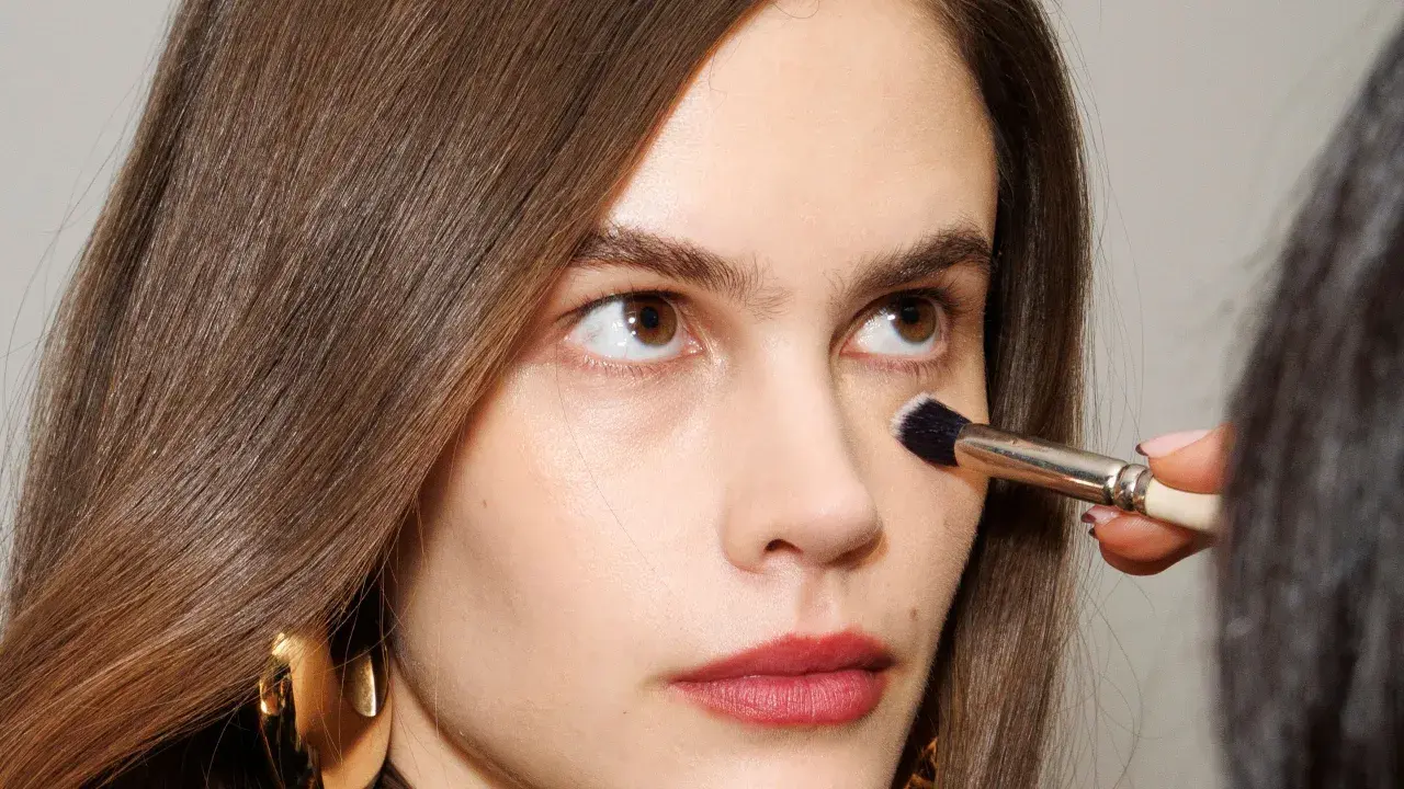 Come capire il colore del correttore online: un primo piano di una donna con pennello da trucco applicato sotto l'occhio.