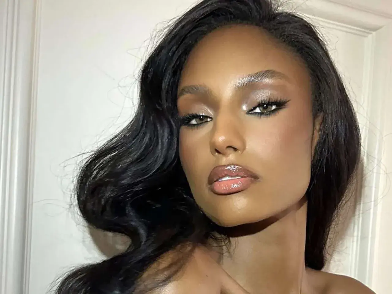 Volto di donna con trucco da sera elegante: occhi definiti da eyeliner e ombretto luminoso, labbra glossate. Capelli scuri e ondulati.