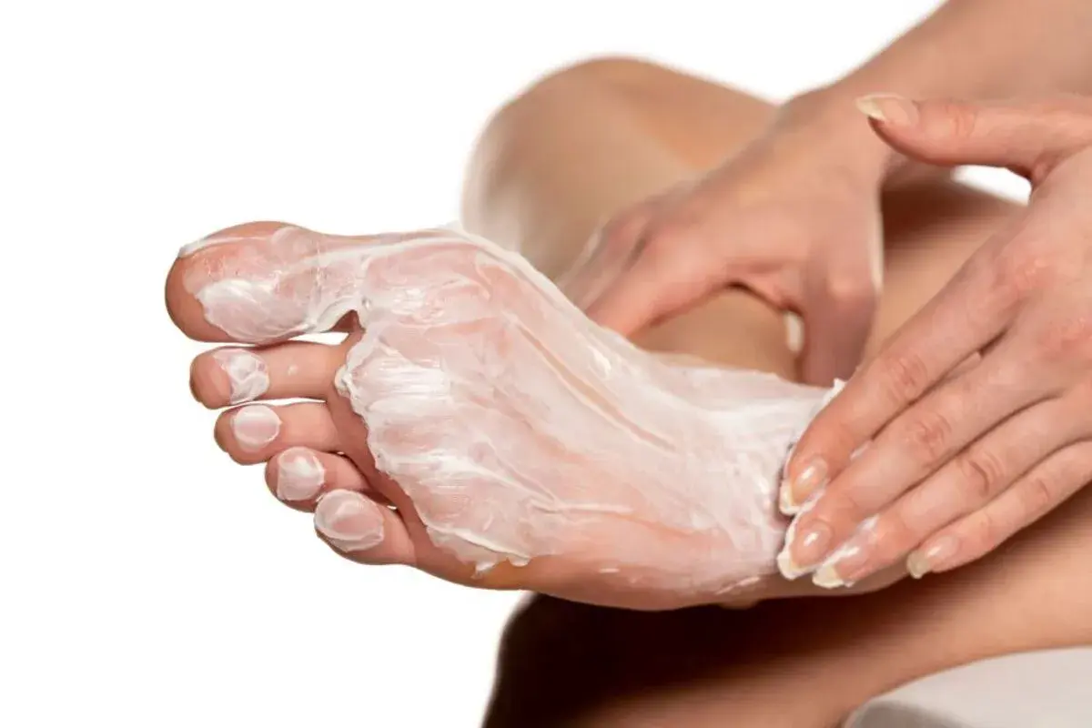 Mani che applicano una crema idratante su un piede, creando un impacco per piedi secchi fai da te per una pelle morbida e nutrita.