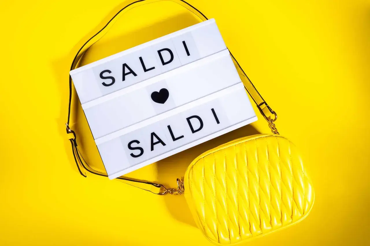 Scatola luminosa con "SALDI" e una borsa gialla. Scopri quanto durano i saldi estivi per fare acquisti convenienti!