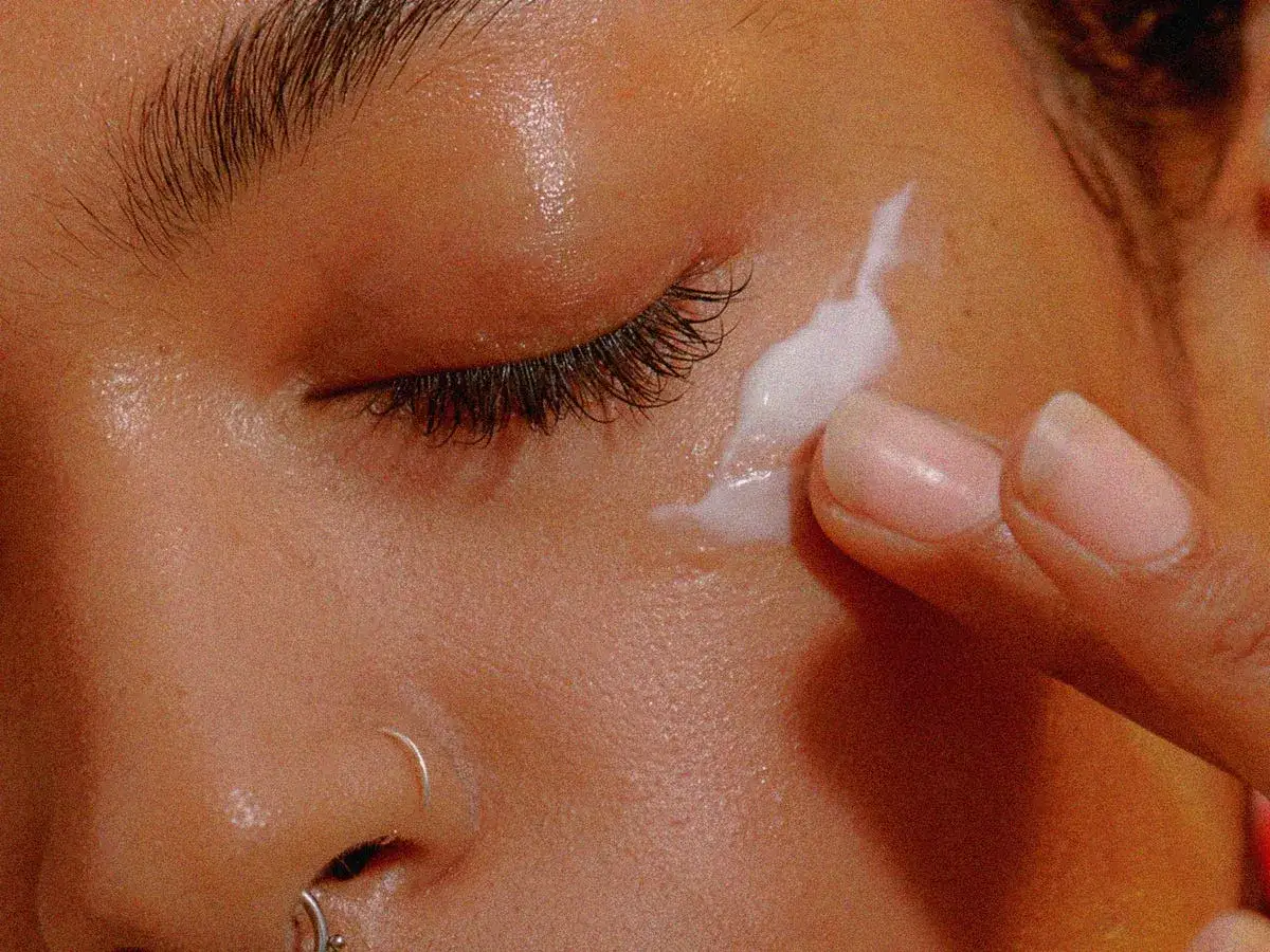 Dita applicano crema su una fronte unta, illuminando la pelle con un tocco di idratazione.