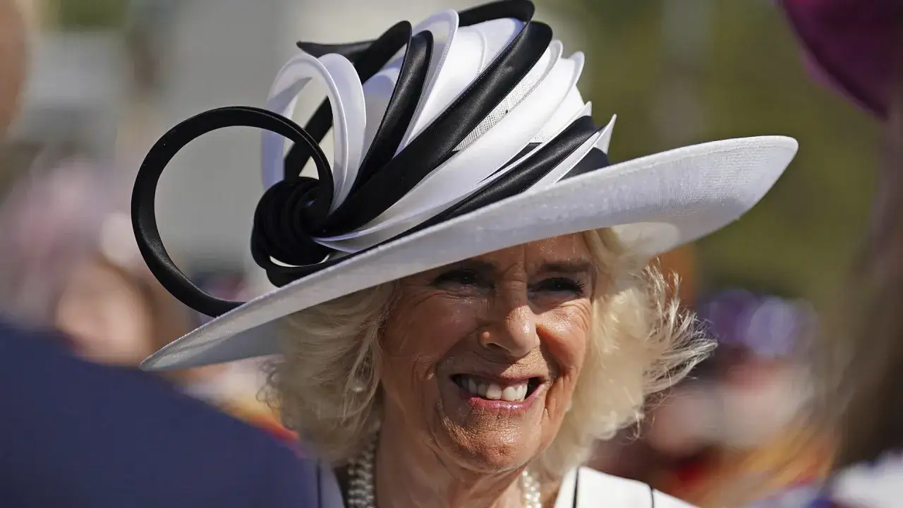 Camilla, regina consorte del Regno Unito, sorride con un cappello bianco e nero audace.
