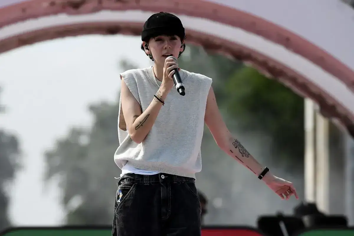 Un ariete cantante con un microfono in mano, indossa un gilet senza maniche e un cappellino nero.