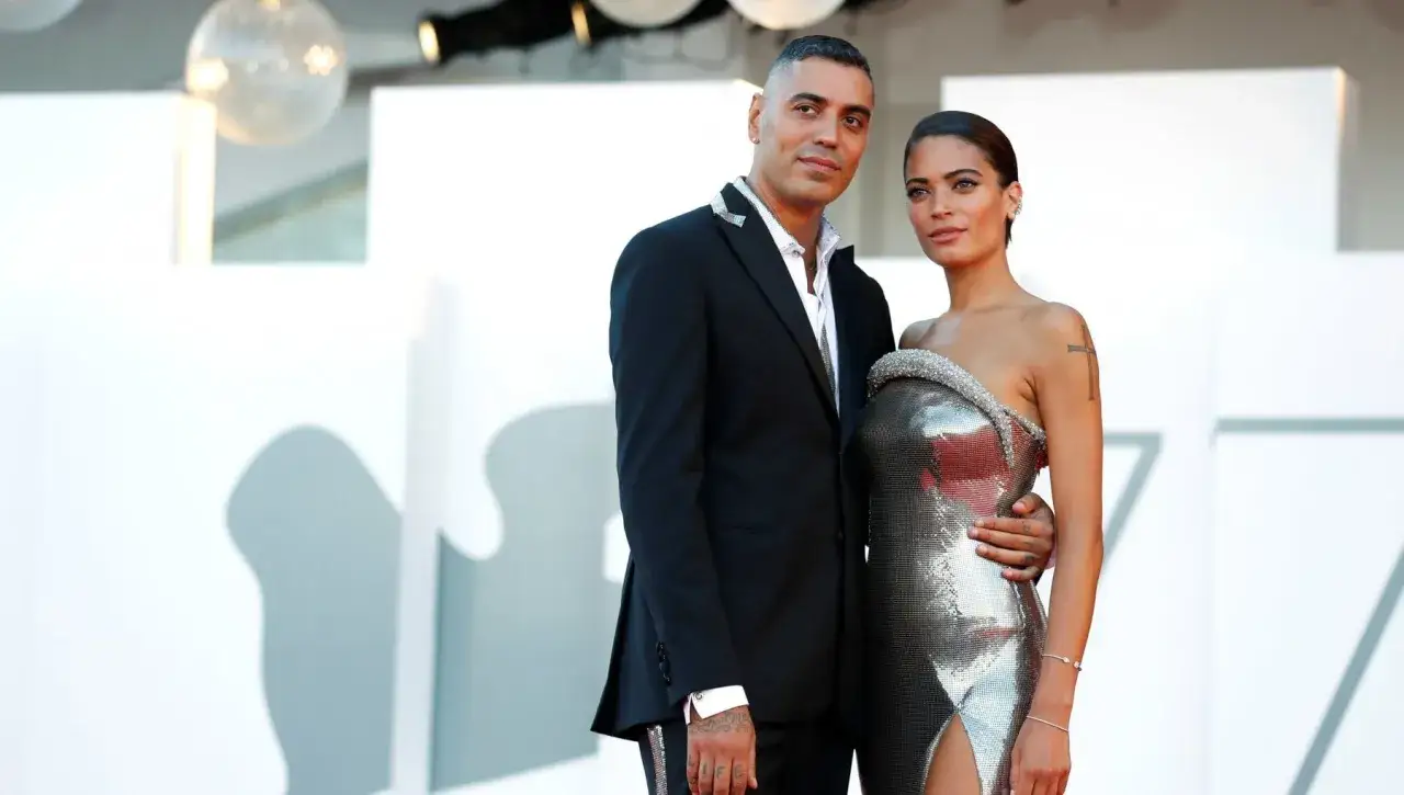 Elodie e Marracash, una coppia di artisti, posano sul red carpet. Lui in completo scuro, lei in abito scintillante.