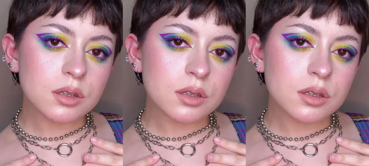 Volto con un audace trucco grafico sugli occhi, con sfumature vivaci di giallo, viola e blu. Indossa collane a catena argentate.