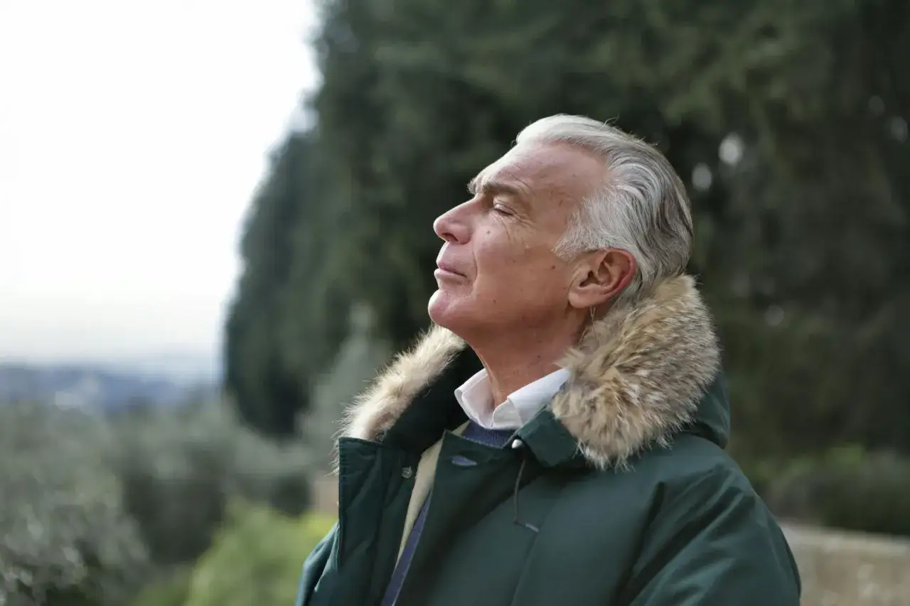 Uomo con occhi chiusi e un sorriso sereno, un modo per alleviare lo stress all'aria aperta.