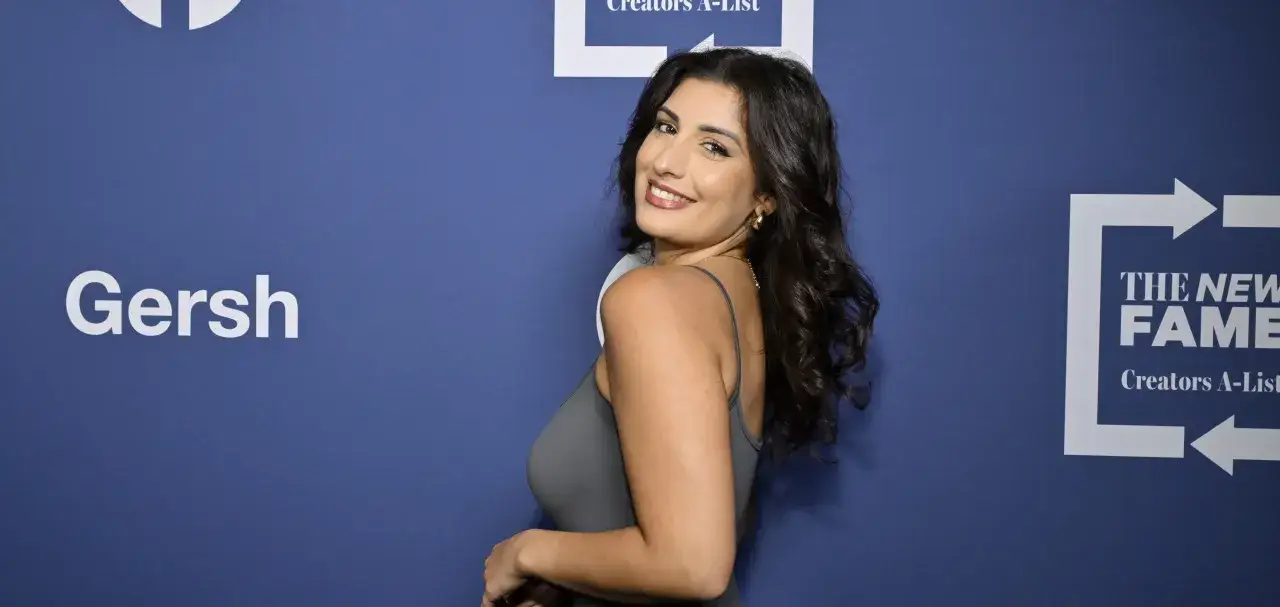 Chiara Frattesi sorride guardando indietro, con i capelli scuri mossi e un abito grigio. Sullo sfondo, i loghi 