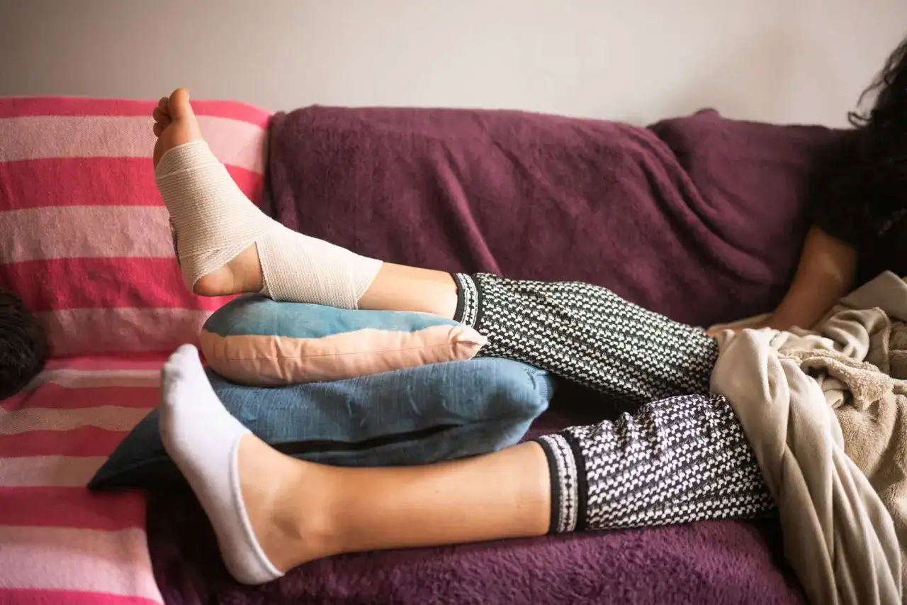 Gambe gonfie e fasciate, riposo sul divano con cuscini per alleviare il dolore. Rimedi gambe gonfie in corso.