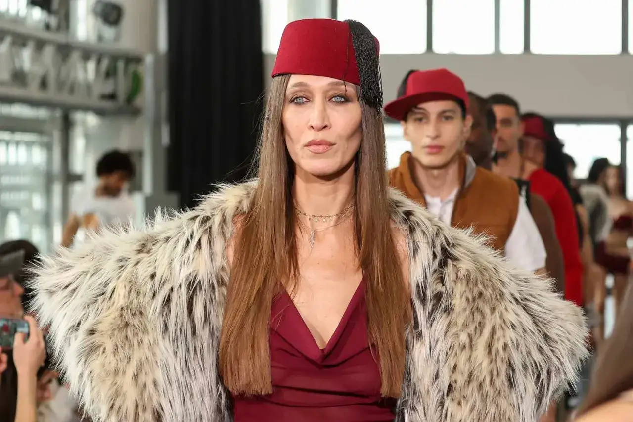 Alana Hadid sfila con un cappello rosso e una pelliccia ecologica, seguita da altri modelli.