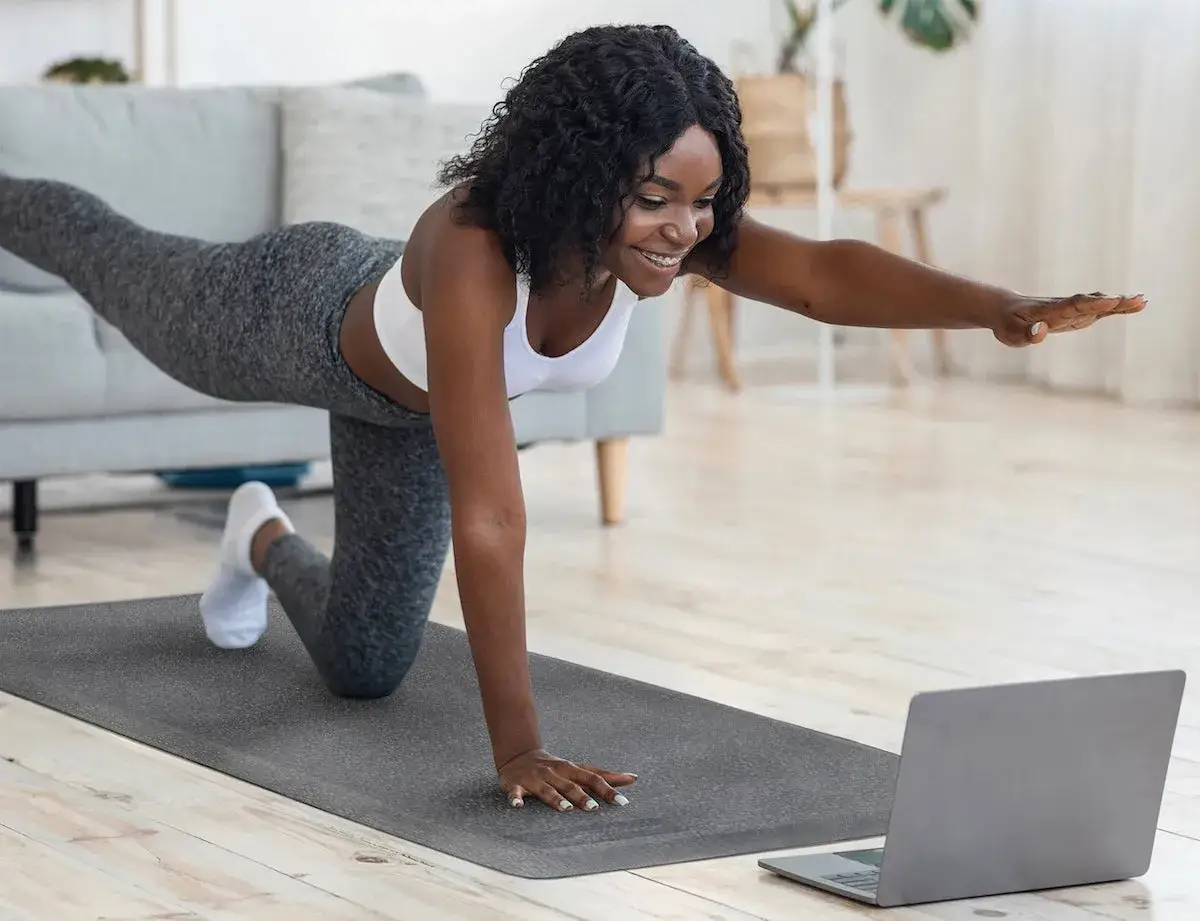 Donna sorridente fa yoga a casa, seguendo un tutorial su laptop. Un allenamento che dimostra come lo yoga fa dimagrire, tonificando il corpo.