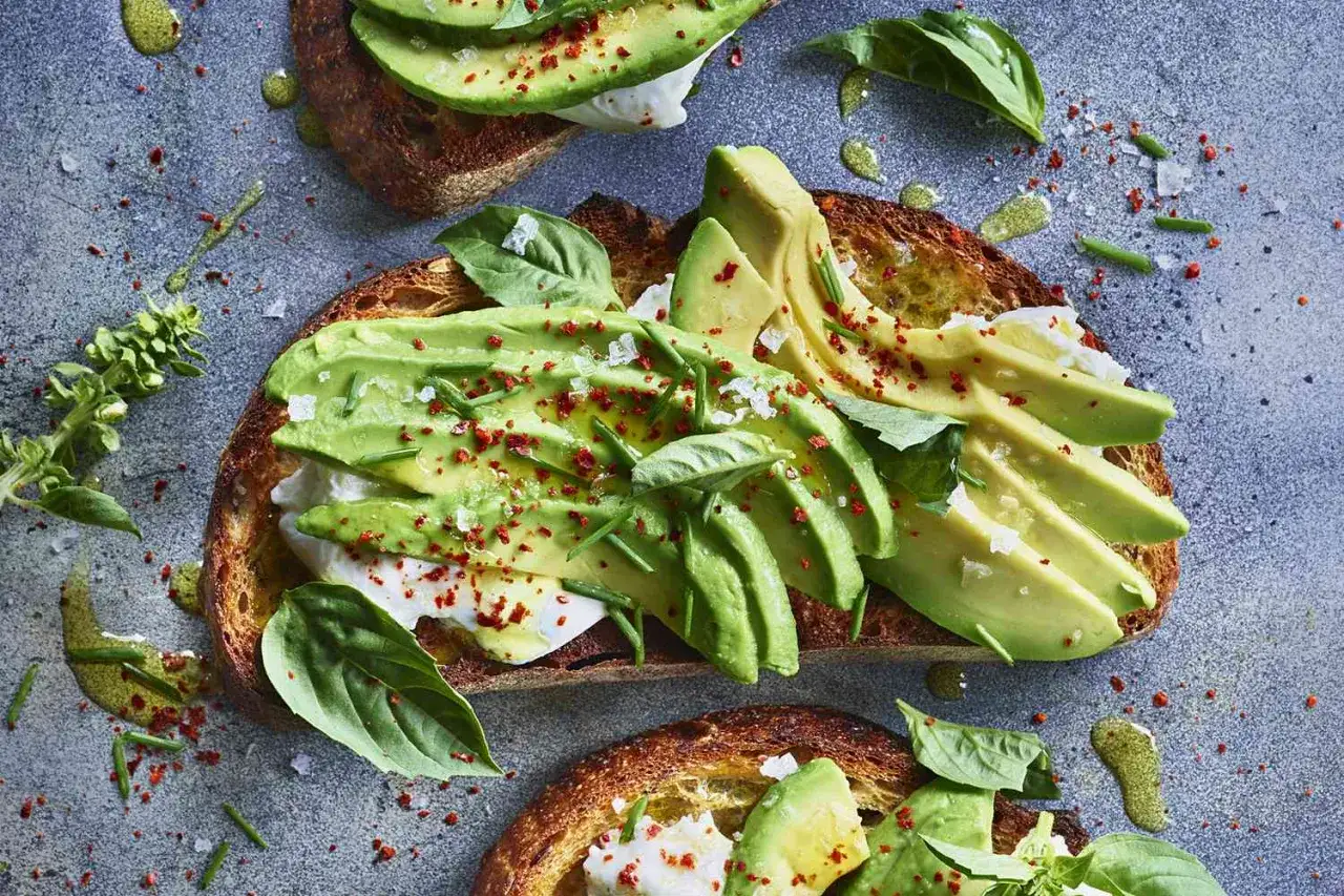 Bruschette con avocado, formaggio fresco e basilico, condite con olio e peperoncino. Perfetto spuntino serale.