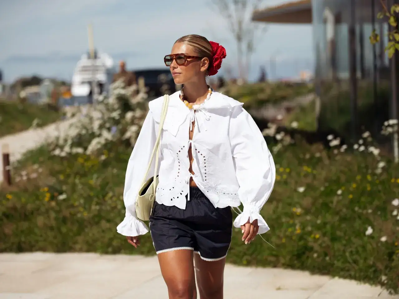 Donna con top bianco con scollo a V e lacci, shorts neri e borsa gialla, passeggia all'aperto.