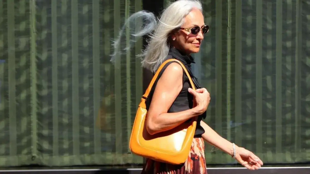 Eleganza senza tempo: una sciura milanese con borsa arancione e capelli al vento, cammina con stile.