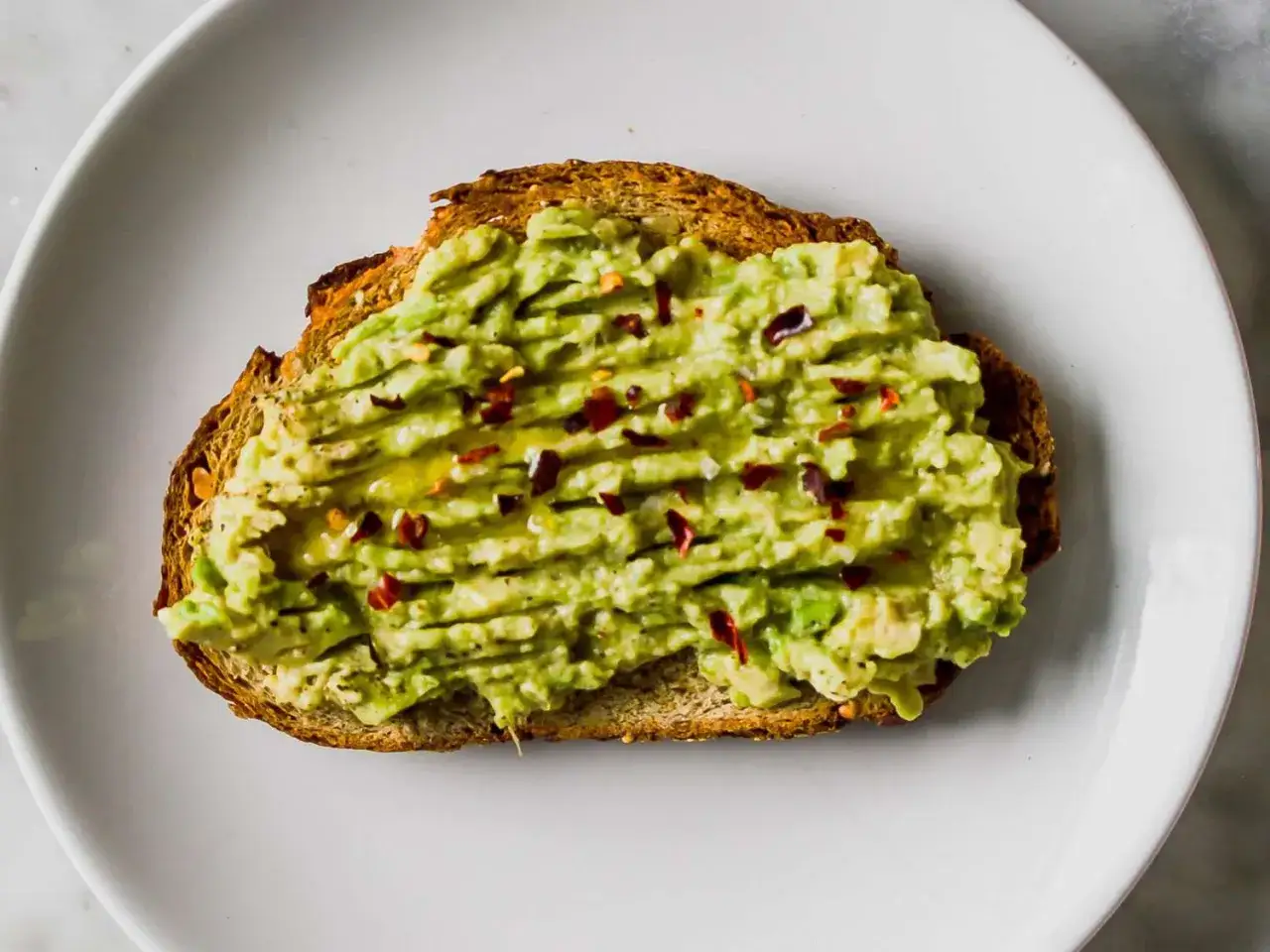Toast integrale con avocado schiacciato, condito con olio e peperoncino. Un concentrato di avocado proprietà per una colazione sana.