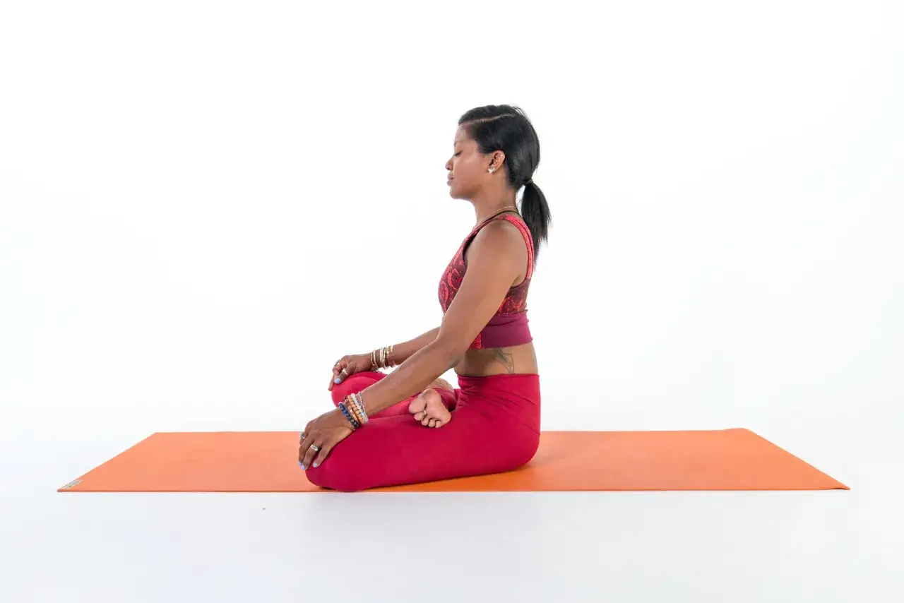 Donna in meditazione su un tappetino arancione, con le gambe incrociate in quella che sembra il fiore di una posizione yoga.