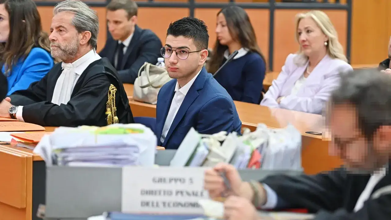 Alex Cotoia, giovane imputato, ascolta in tribunale. Al suo fianco, avvocati e giudici in toga.
