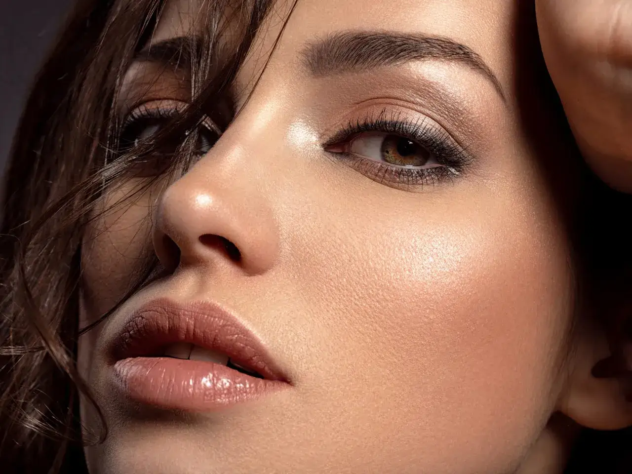 Primo piano di un volto femminile con un trucco da sera elegante, labbra lucide e occhi intensi.