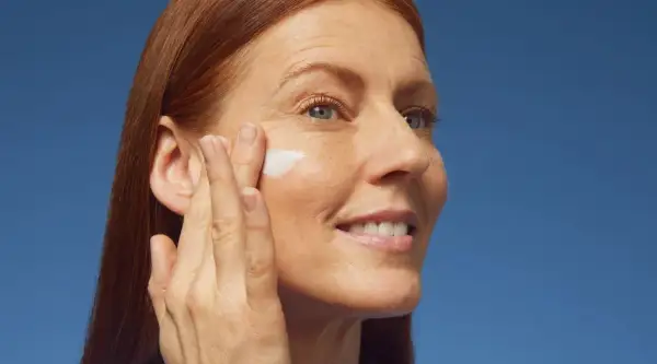 Donna con capelli rossi applica crema sul viso, contrastando la desquamazione della pelle.