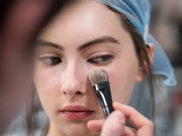 Una mano applica il fondotinta sul viso di una modella con un pennello. Ecco come applicare il fondotinta per un look impeccabile.