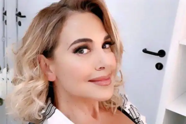 Barbara D'Urso sorride con capelli biondi mossi e trucco accentuato.