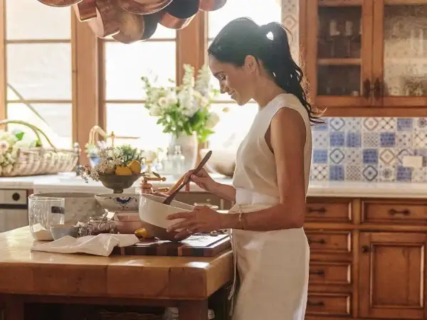 Meghan, Duchessa di Sussex, sorride mentre mescola in una ciotola in una cucina luminosa.
