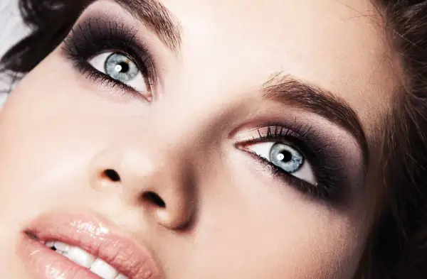 Occhi azzurri con un intenso trucco smokey eyes, labbra lucide e pelle luminosa.