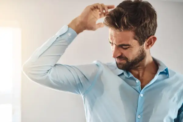 Uomo con camicia bagnata di sudore, preoccupato per le cause del sudore acido.
