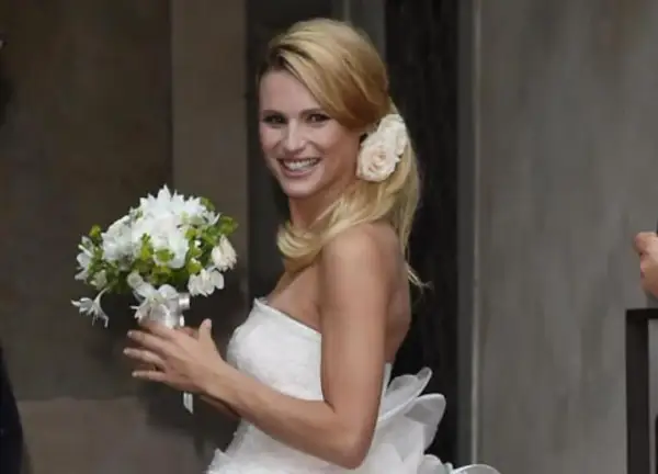 Michelle Hunziker sorride con un bouquet, indossando un abito da sposa che ricorda quello del suo matrimonio con Eros Ramazzotti.