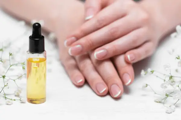 Olio per unghie e cuticole secche, con mani curate e fiori bianchi.