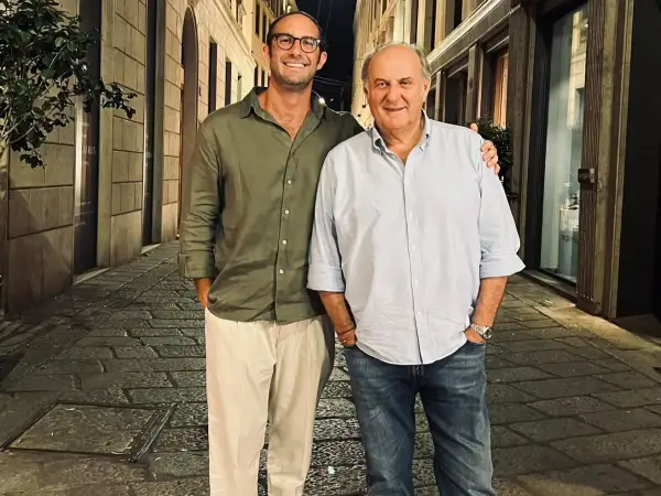 Edoardo Scotti sorride con un amico in una strada acciottolata di sera.