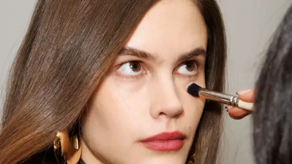 Come capire il colore del correttore online: un primo piano di una donna con pennello da trucco applicato sotto l'occhio.