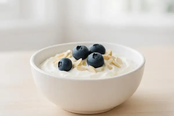 Una ciotola di yogurt bianco con mirtilli e mandorle a lamelle, perfetta per uno spuntino serale leggero e nutriente.