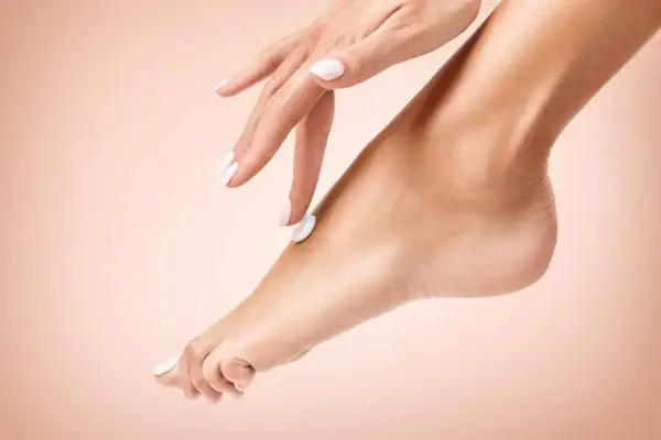 Mano con unghie bianche applica crema su un piede, un gesto di cura per un perfetto pedicure fai da te.