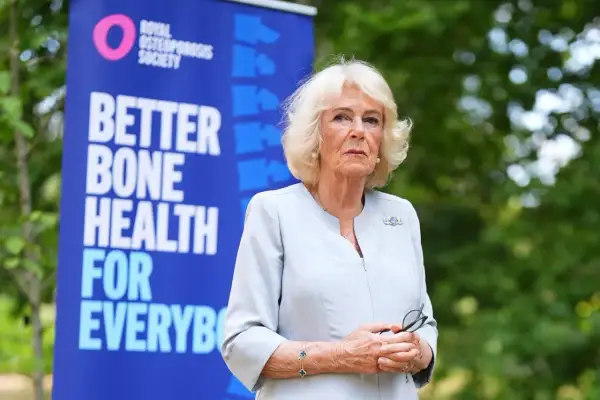 Camilla, regina consorte del Regno Unito, sorride con un banner della Royal Osteoporosis Society alle spalle.