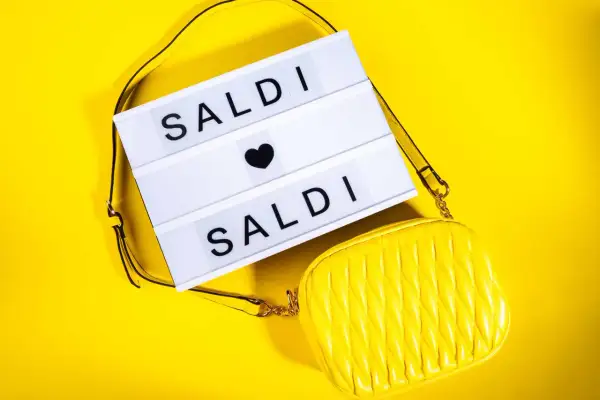 Scatola luminosa con "SALDI" e una borsa gialla. Scopri quanto durano i saldi estivi per fare acquisti convenienti!