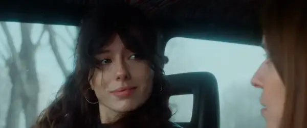 Ragazza con capelli scuri e orecchini a cerchio, guarda fuori dal finestrino, il cielo è celeste dalla porta.